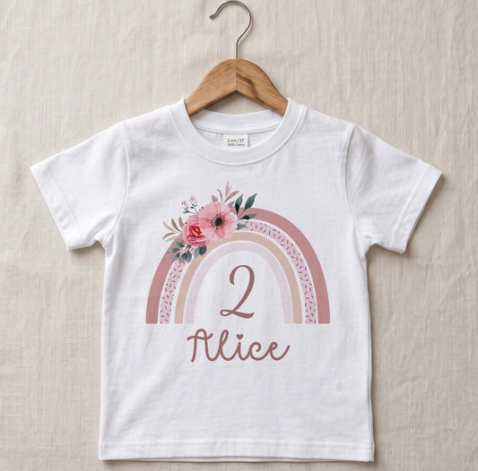 T-shirt enfant personnalisé pour anniversaire suspendu sur un cintre en bois, motif arc-en-ciel bohème fleuri rose avec le chiffre 2 et le prénom Alice floqués en flex rose gold
