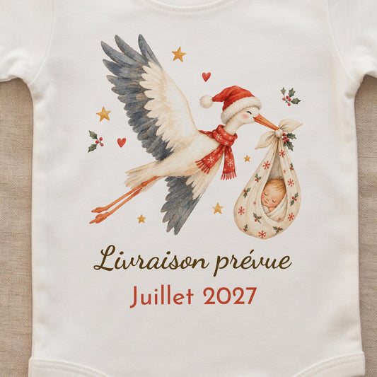 Gros plan sur l'impression du body : cigogne de Noël aquarelle avec bonnet et écharpe rouge, bébé endormi dans un baluchon à flocons et houx, texte Livraison prévue Juillet 2027