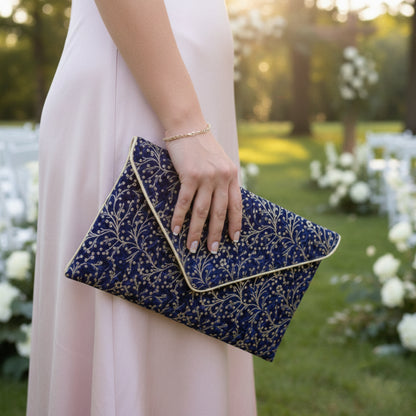 Pochette mariage bleu marine et dorée en tissu brocart portée à la main avec une robe rose poudré