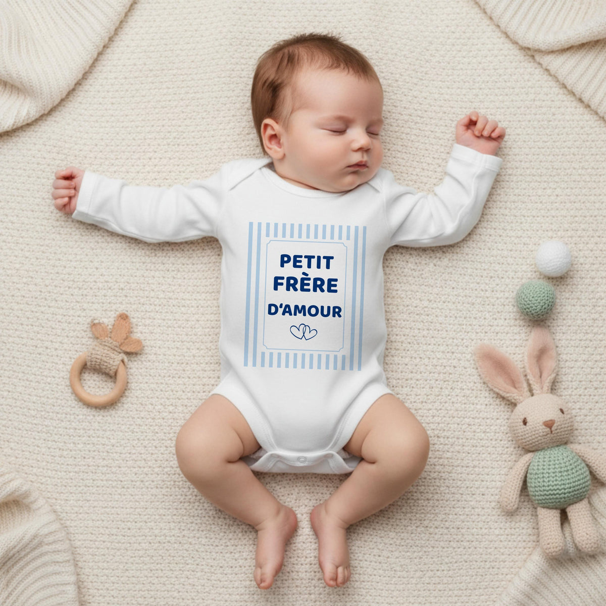 Bébé endormi dans un body blanc manches longues Petit frère d'amour à rayures bleu ciel, sur une couverture en tricot crème avec doudou lapin