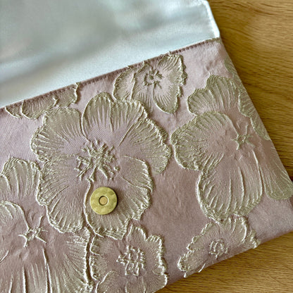 Vue détaillée de la pochette Fil des Toiles en brocart rose : texture relief des fleurs, reflets satinés et format rectangulaire élégant.