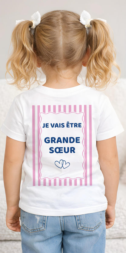 T-shirt enfant blanc future grande sœur, dos avec l'inscription Je vais être grande sœur dans un cadre rose à rayures et deux cœurs entrelacés