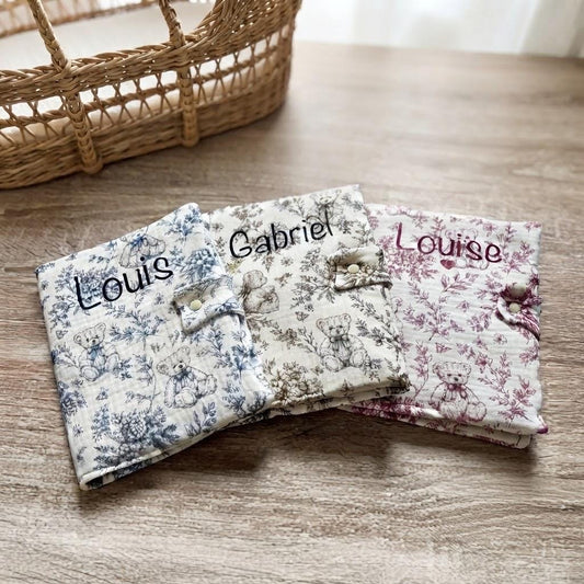 Trois protège carnets de santé en gaze de coton motif toile de Jouy oursons, coloris bleu, marron et bordeaux, personnalisés aux prénoms Louis, Gabriel et Louise, avec un cœur sous Louise