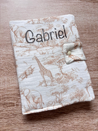 Protège carnet de santé beige en gaze de coton motif toile de Jouy Safari avec girafe et éléphants, personnalisé au prénom Gabriel en flocage marron chocolat, fermeture par patte à bouton pression