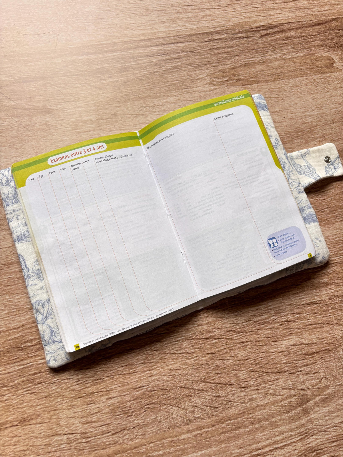 Protège carnet de santé bleu en gaze de coton motif toile de Jouy Safari ouvert, avec le carnet de santé glissé dans les rabats intérieurs blancs et la patte à bouton pression