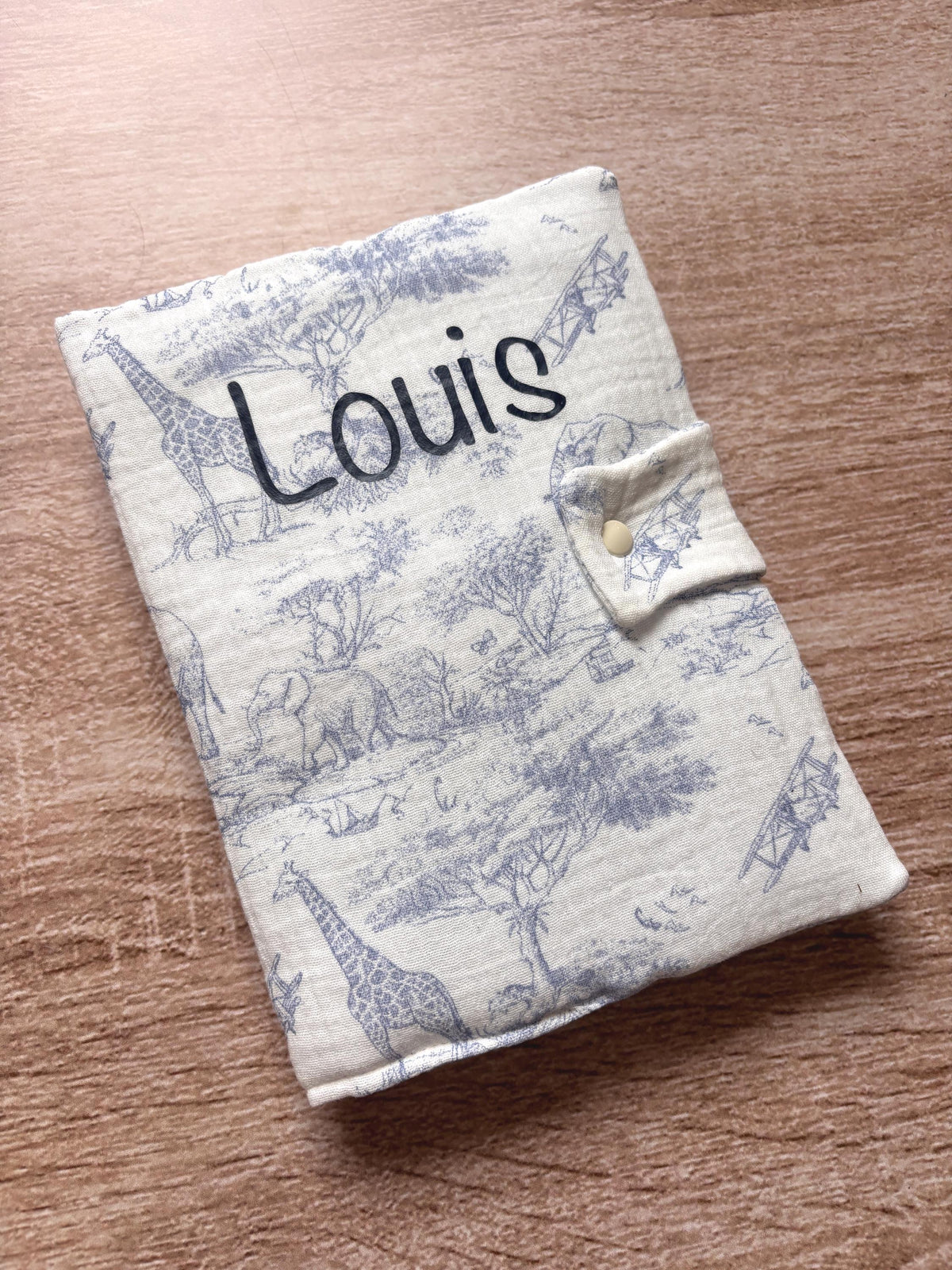 Protège carnet de santé bleu en gaze de coton motif toile de Jouy Safari avec girafes, éléphants et avions anciens, personnalisé au prénom Louis en flocage bleu marine