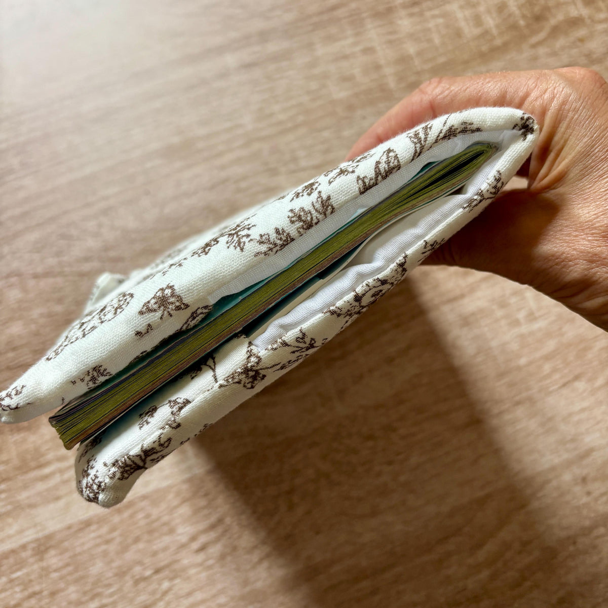 Vue de profil du protège carnet de santé molletonné en gaze de coton, avec le carnet de santé glissé dans les rabats intérieurs blancs