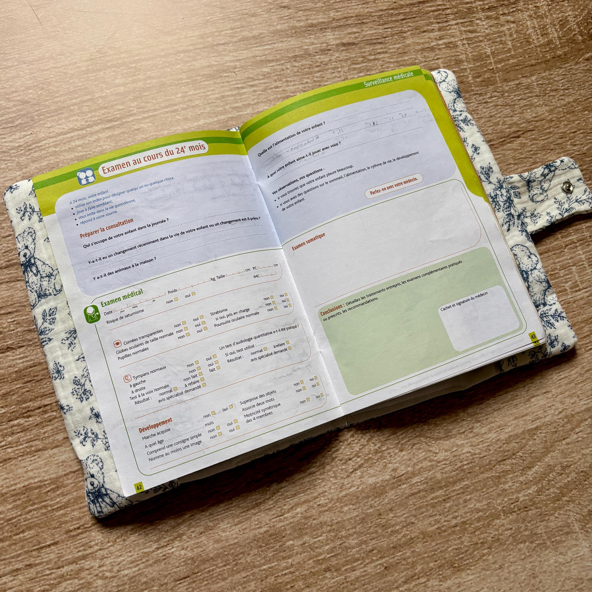 Protège carnet de santé en gaze de coton motif toile de Jouy oursons ouvert, avec le carnet de santé glissé à l'intérieur et la patte à bouton pression