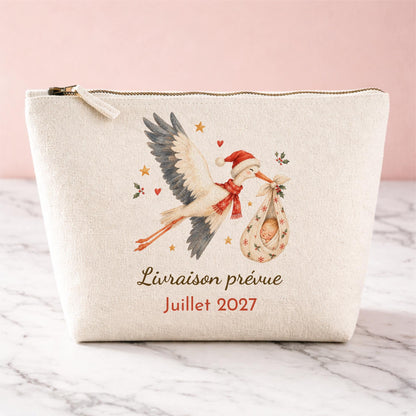 Trousse en coton naturel personnalisée pour annonce de grossesse à Noël : cigogne aquarelle en bonnet de Noël portant bébé dans un baluchon, texte Livraison prévue Juillet 2027
