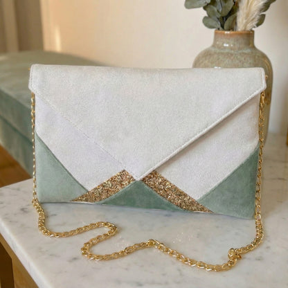 Pochette femme format enveloppe en suédine blanche, velours vert sauge, paillettes dorées avec chaîne dorée posée sur une table