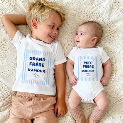 Grand frère et bébé allongés face à face, t-shirt blanc Grand frère d'amour et body blanc Petit frère d'amour, cadre à rayures bleu ciel et deux cœurs