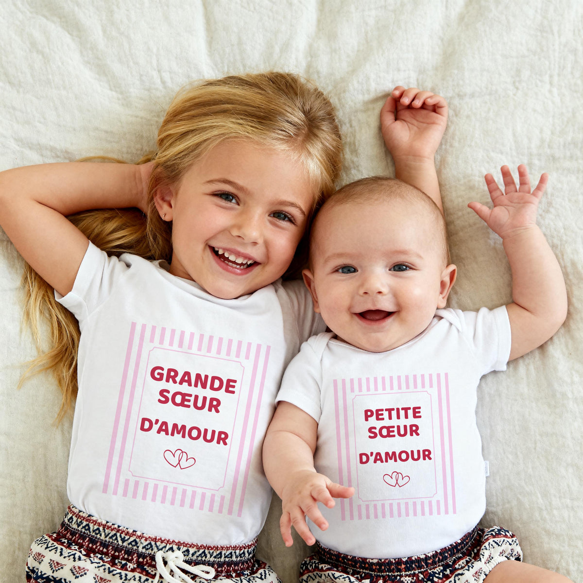 Grande sœur et petite sœur allongées côte à côte, t-shirt blanc Grande sœur d'amour et body blanc Petite sœur d'amour, cadre à rayures roses et deux cœurs
