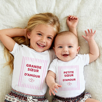 Grande sœur et petite sœur allongées côte à côte, t-shirt blanc Grande sœur d'amour et body blanc Petite sœur d'amour, cadre à rayures roses et deux cœurs