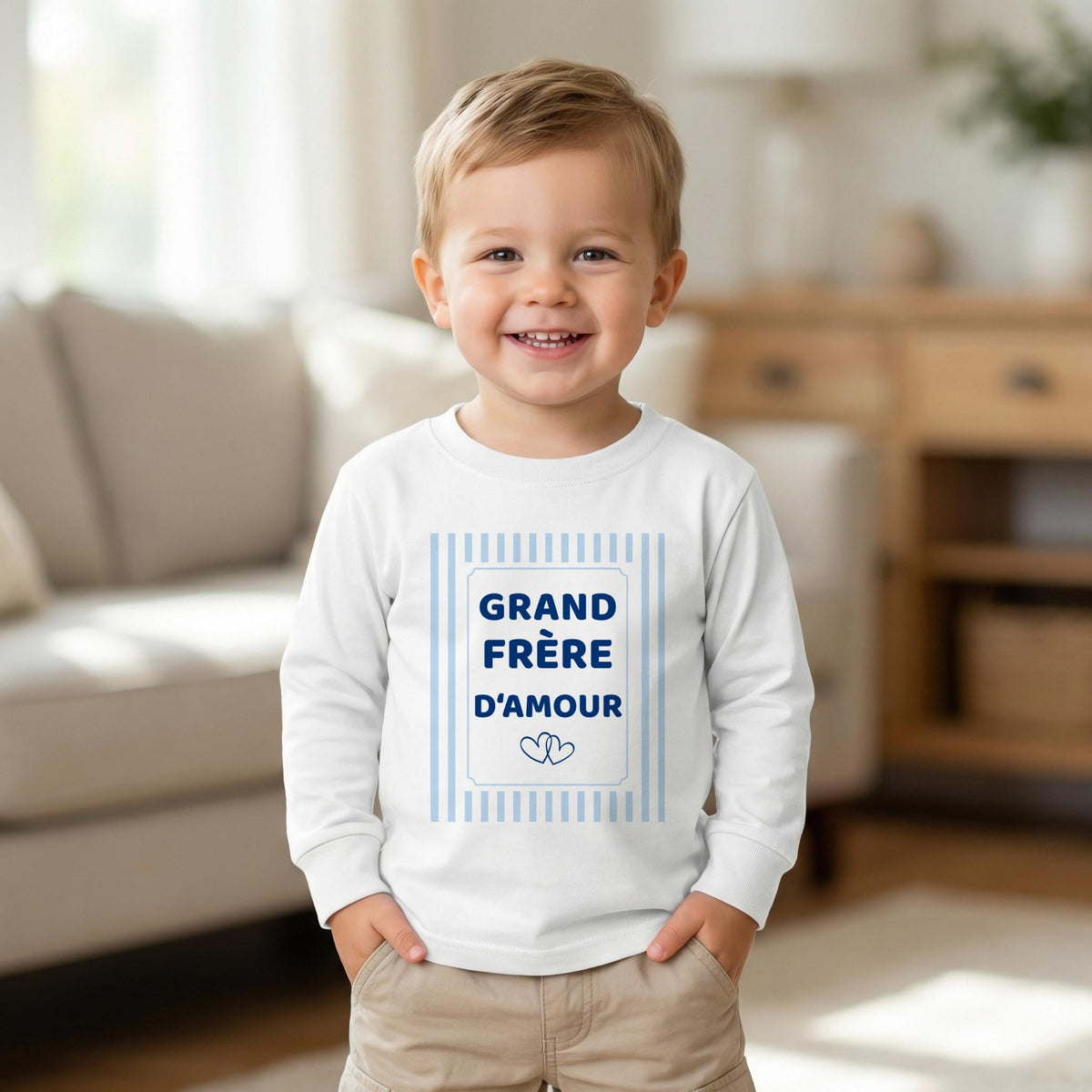 Petit garçon souriant, mains dans les poches, vêtu d'un t-shirt blanc manches longues Grand frère d'amour, cadre à rayures bleu ciel et deux cœurs
